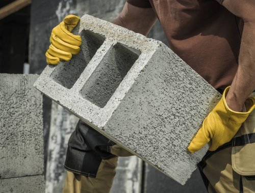 Caucasian Construction Contractor Worker Moving Modern Hollow Dense Concrete Block Along Construction Site.