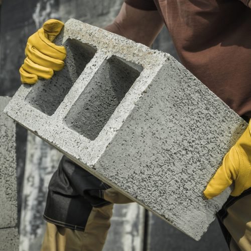 Caucasian Construction Contractor Worker Moving Modern Hollow Dense Concrete Block Along Construction Site.